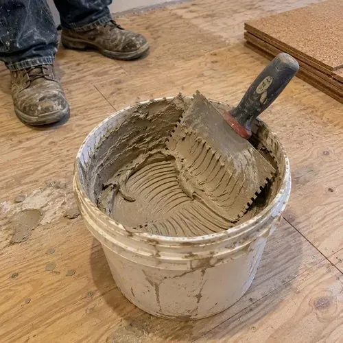 Cork adhesive tub and notched trowel on subfloor during cork floor installation