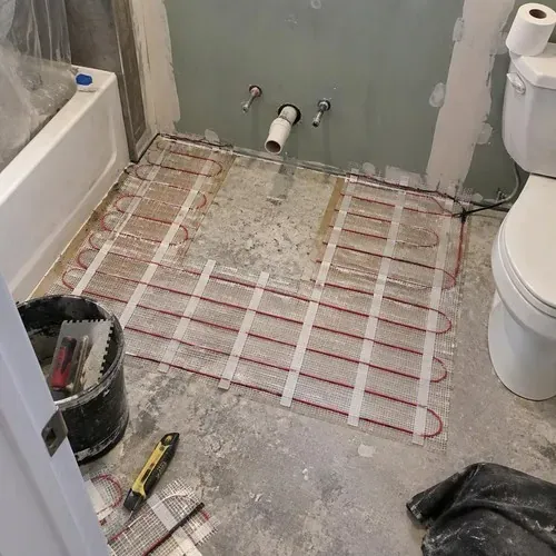 Electric heating mat fitted around vanity footprint during radiant heated floor installation